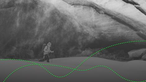Skitourengeher mit Rucksack und Stöcken vor Felswand, darüber grüne Linie