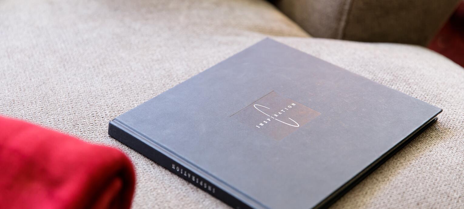 Buch mit dem Titel Inspiration liegt auf einem beigen Sofa neben einem roten Kleidungsstück