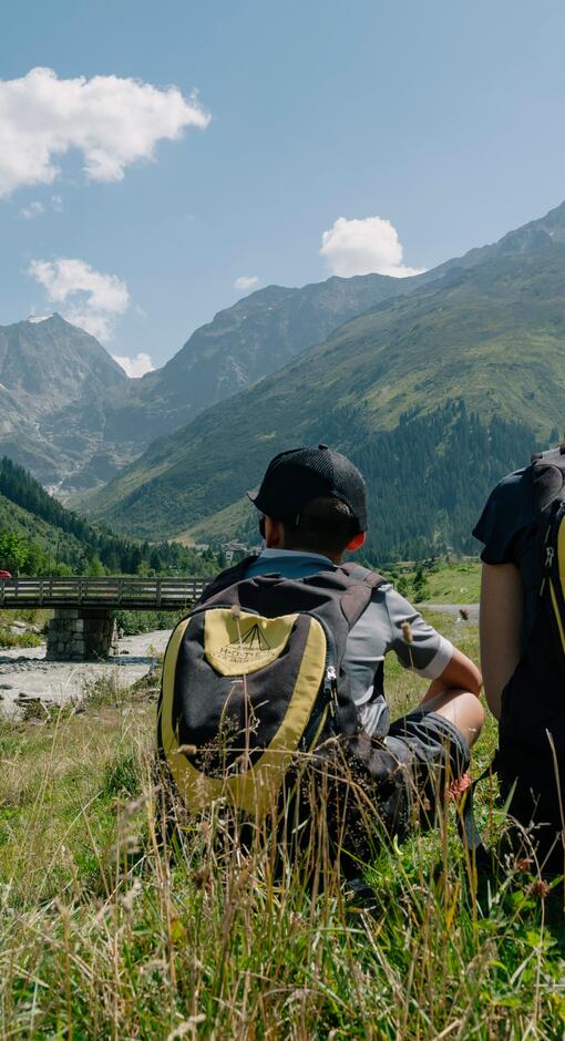 Two children are sitting outside the DAS VIER hotel, gazing at the mountains