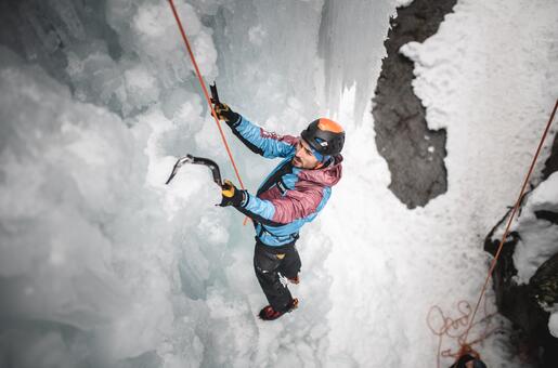 Eiskletterer mit Helm und Steigeisen an gefrorenem Wasserfall mit Seil