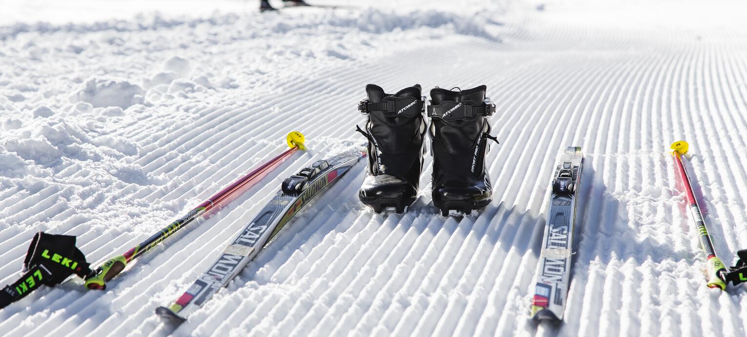 Langlaufski, Stöcke und Schuhe liegen auf präparierter Schneefläche