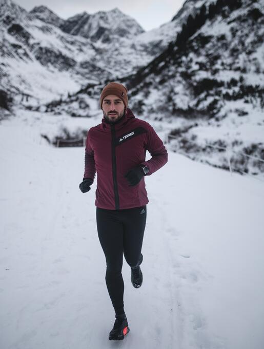 Mann joggt im Schnee vor Bergkulisse mit Mütze und Sportkleidung
