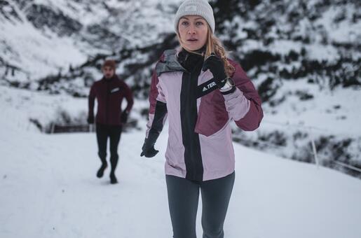 Woman jogging in the snow, man in the background, snowy mountains