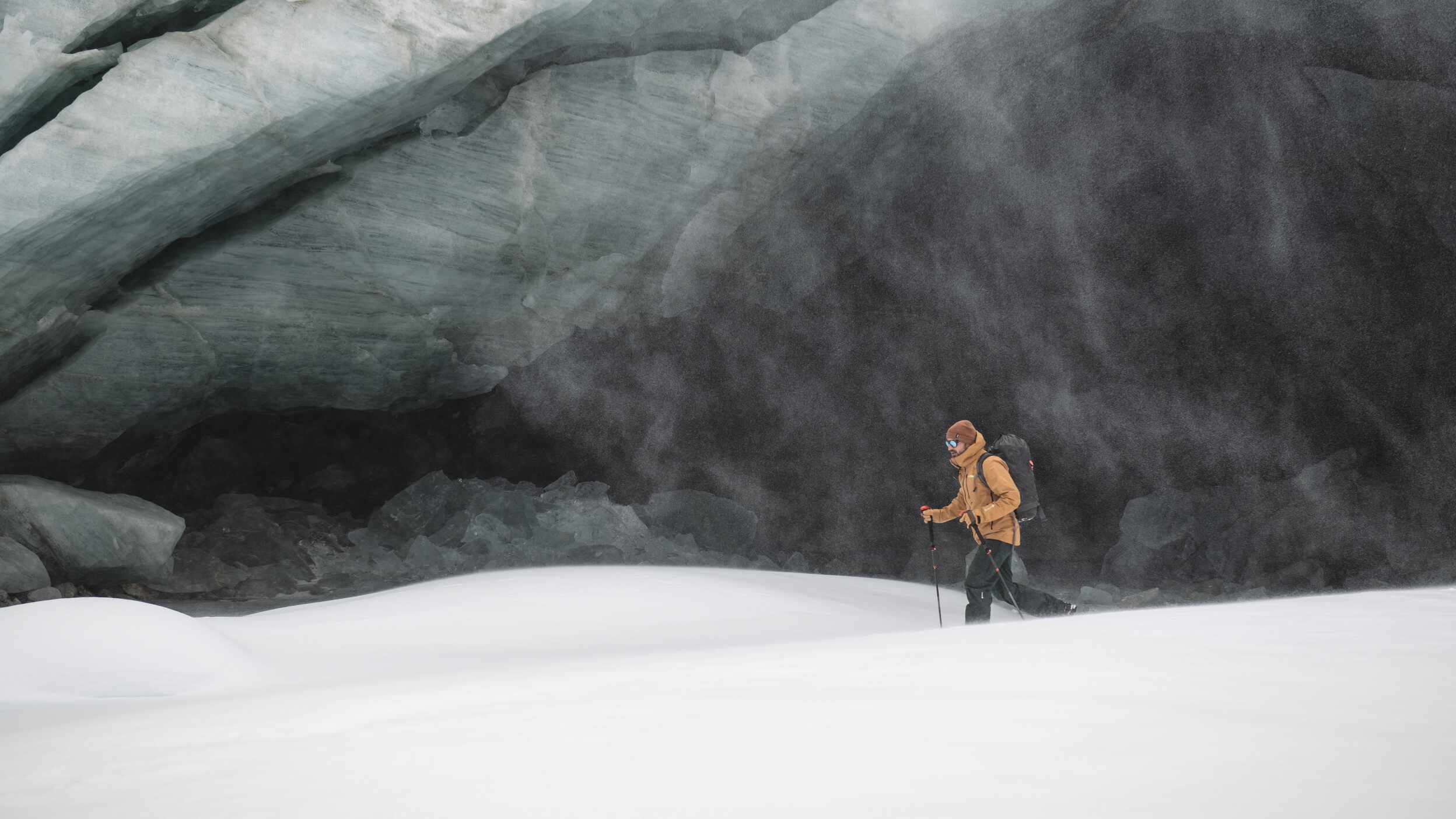 Wanderer mit Rucksack und Stöcken vor eisiger Höhle im Schnee