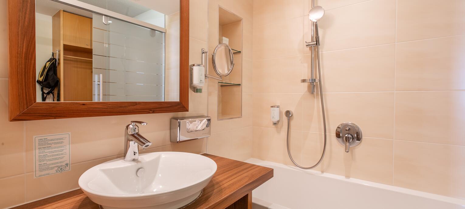 Badezimmer mit Waschbecken auf Holzplatte, Spiegel, Badewanne und Dusche