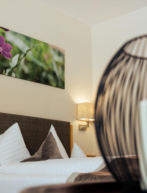 Hotelzimmer mit Doppelbett, Wandbild und dekorativer Lampe im Vordergrund